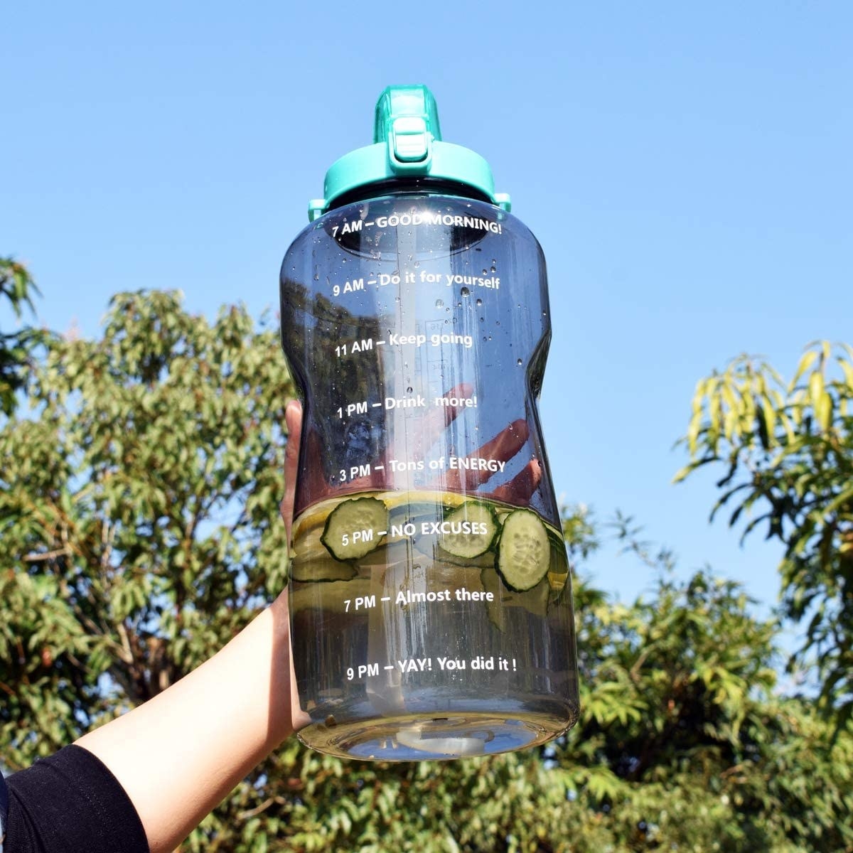 A person holding a large water bottle with sliced cucumbers inside