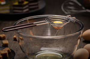an egg yolk sitting in the soleader yolk separator which hangs over a bowl