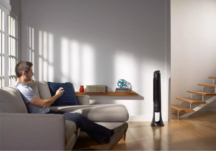 a person aiming a remote at the tower fan in a living room