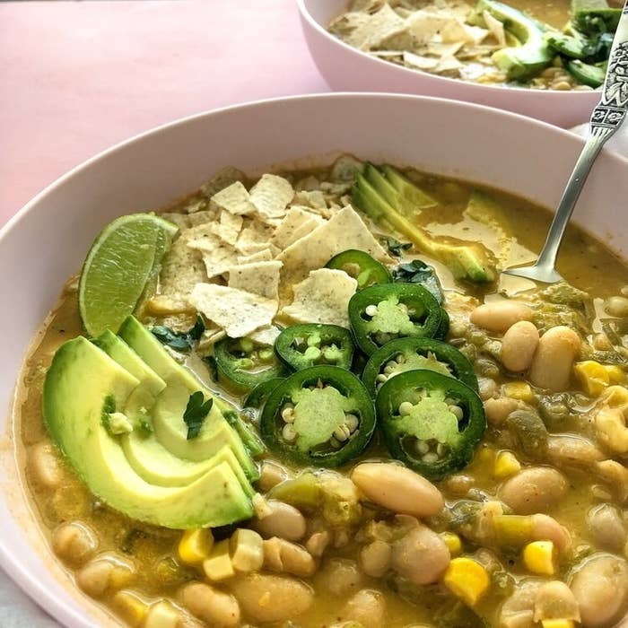 A bowl of white bean chili with tortillas, jalapeño, and avocado.