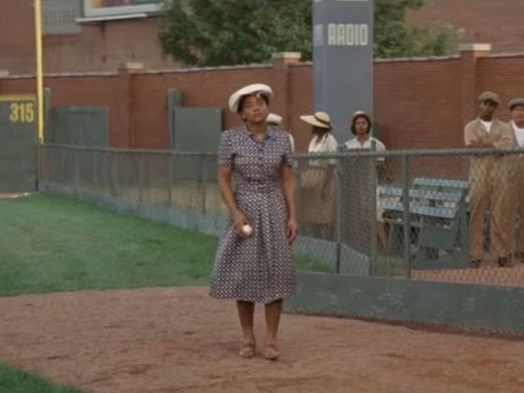 A black woman holding a baseball while walking onto the field 