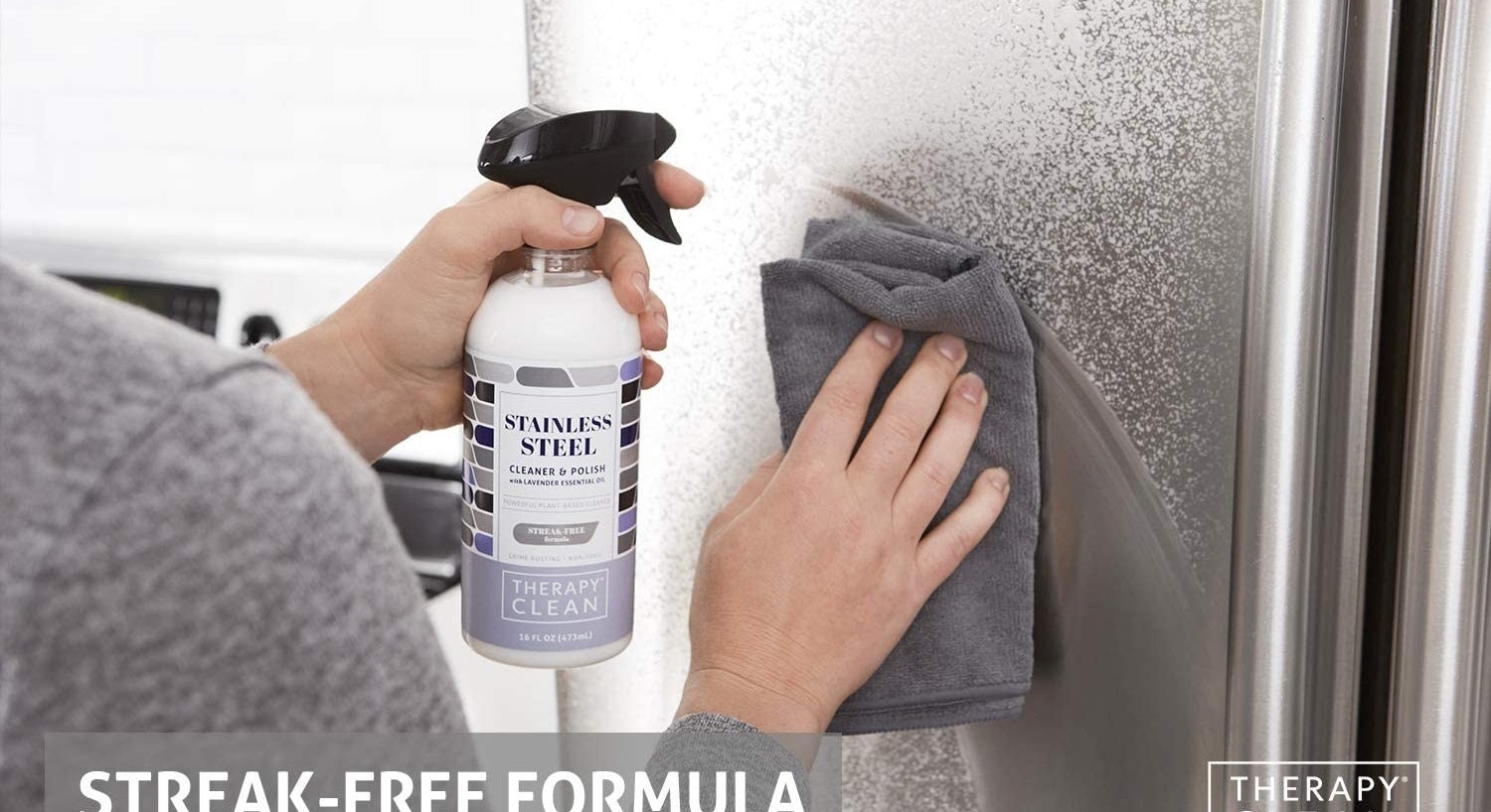 Hands spraying the white cleaner on a fridge, then wiping with a microfiber cloth