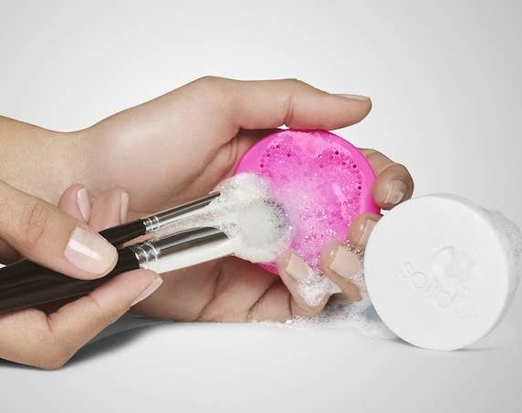 A person washing two makeup brushes with the cleanser and scrubbing pad