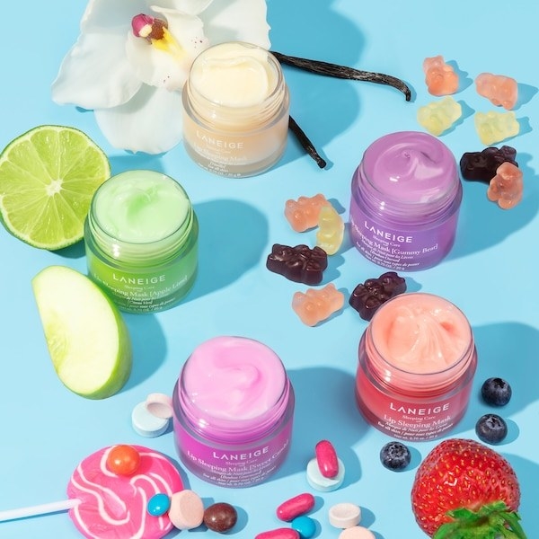 Multiple jars of the lip mask shown with candies and fruit scattered around them