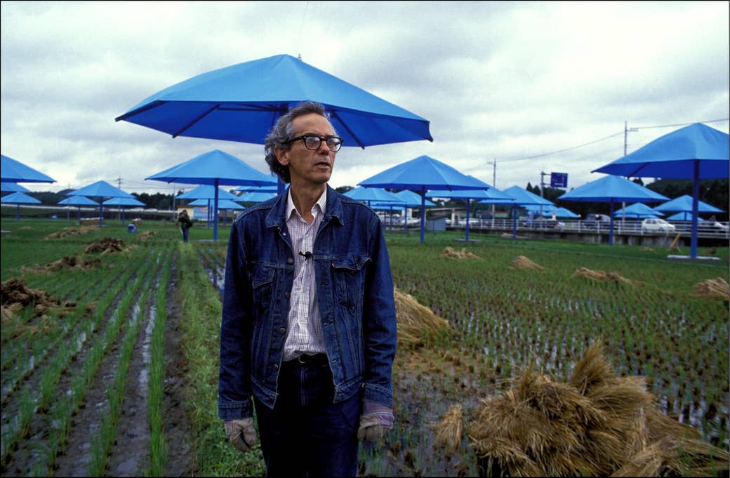 Man in denim jacket in a field with blue umbrellas behind him