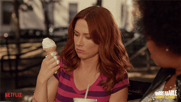 A person licking ice cream off their fingers while holding an ice cream cone
