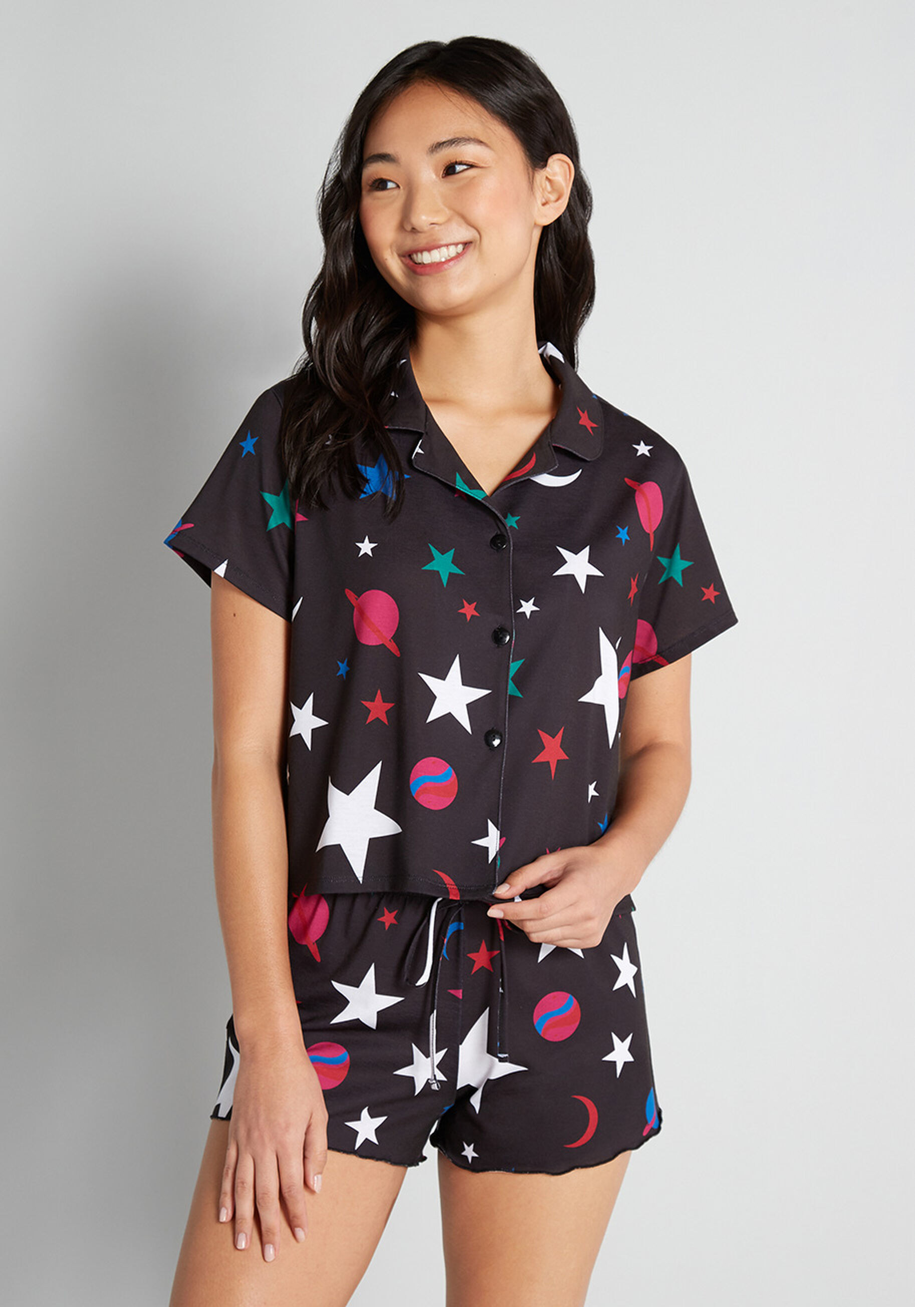 a model wearing a black pajama set with white stars and red and blue planets on it
