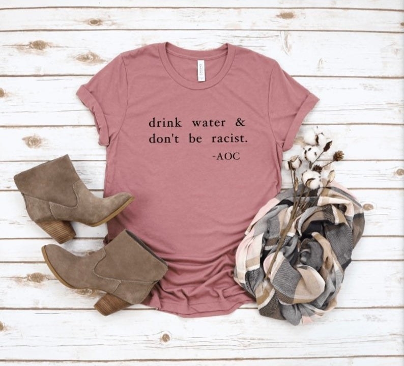 A t-shirt that says &quot;drink water and don&#x27;t be racist,&quot; a quote by AOC. 