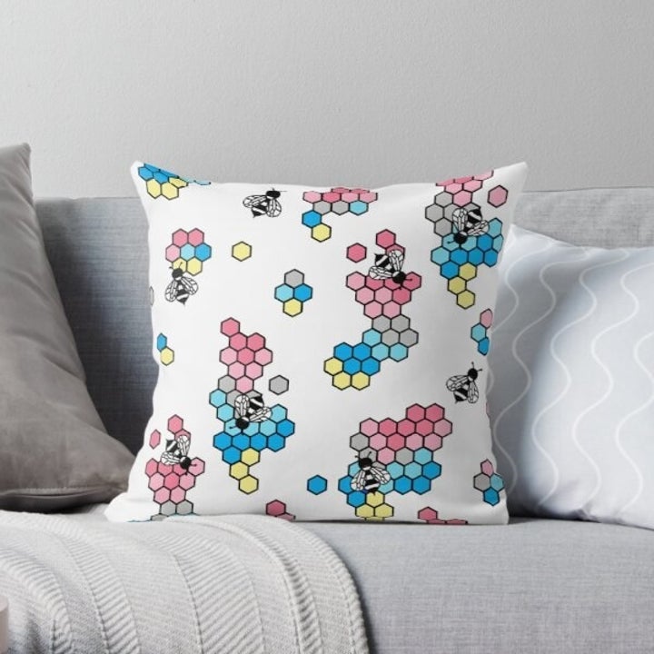 the square pillow with the bees and the gender flux pride colors on the beehives (yellow, pink, gray, and blue)