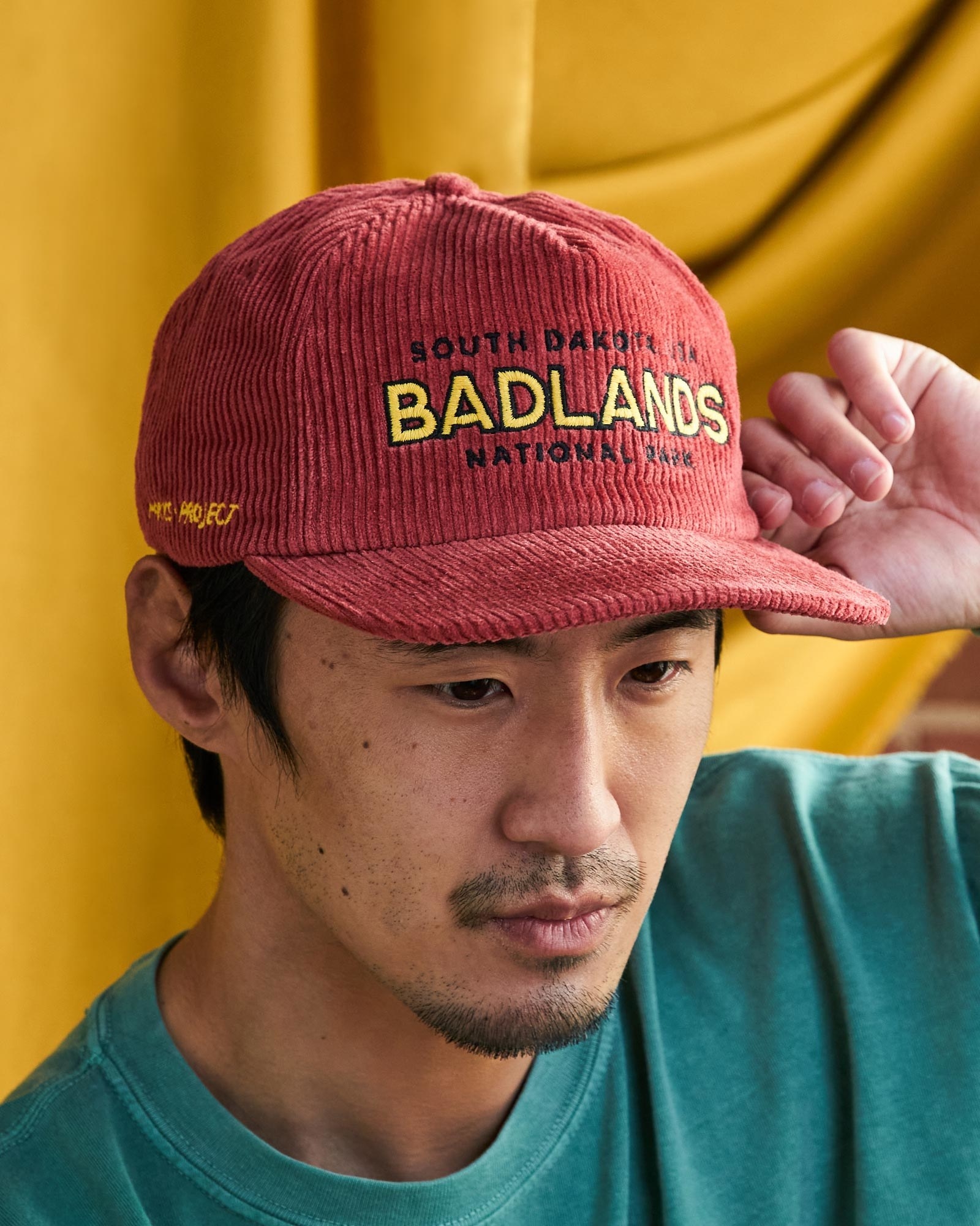 Model wearing red cord hat with "South Dakota Badlands National Park" embroidered onto it