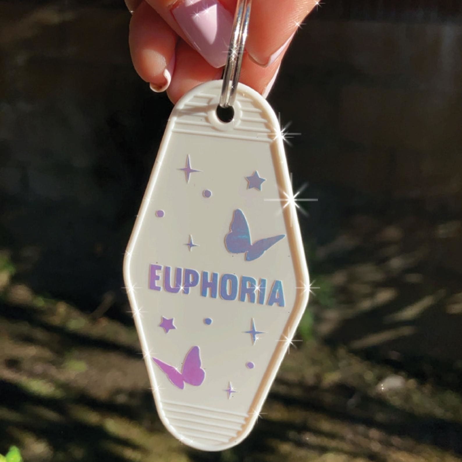 a hand dangles the euphoria holographic vintage keychain