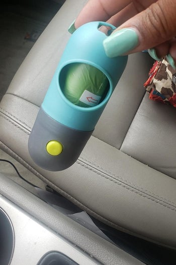 Reviewer photo of a hand holding the blue and gray poop bag dispenser filled with bags 