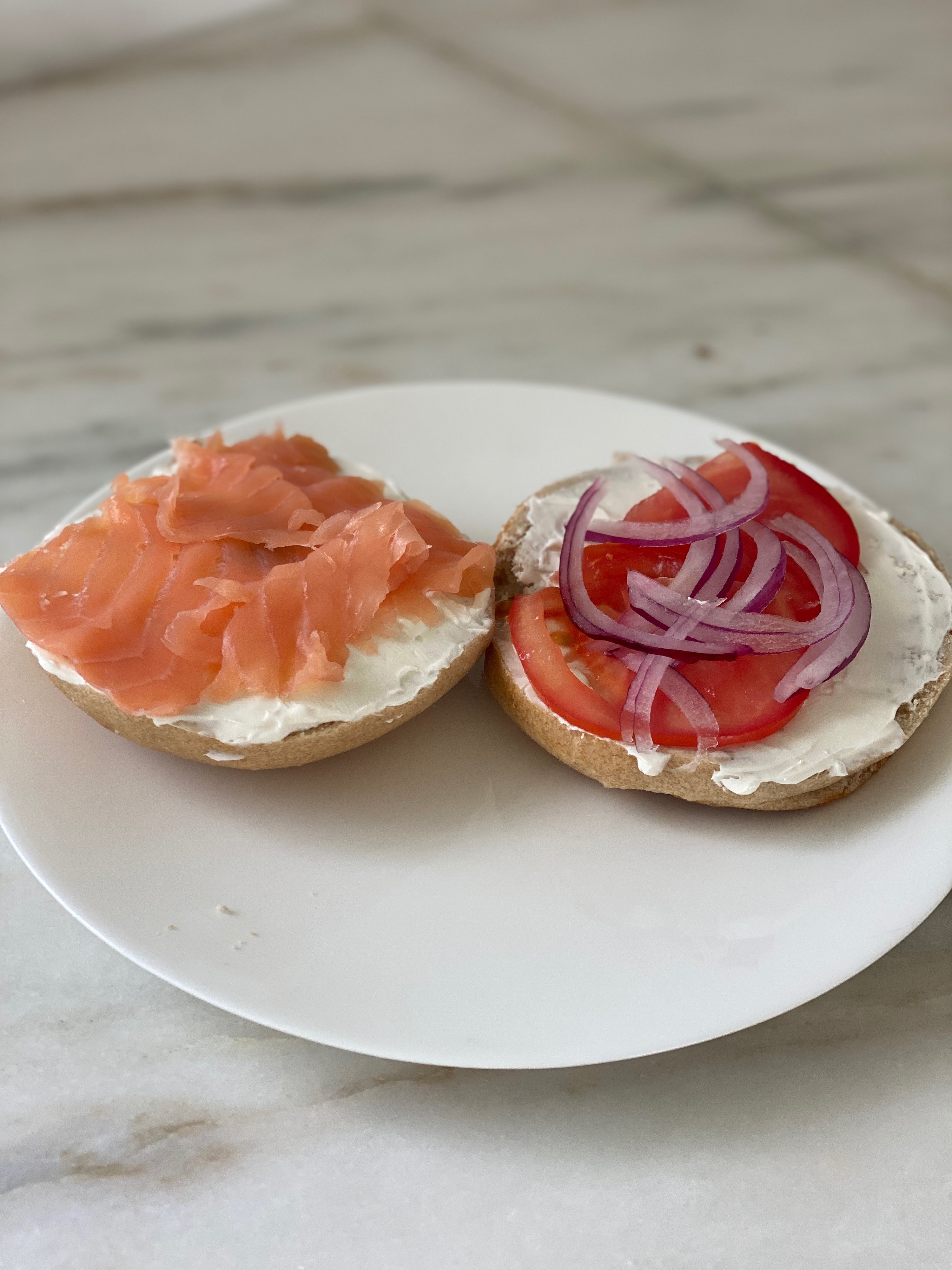 A bagel topped with cream cheese, lox, tomato, and red onion.