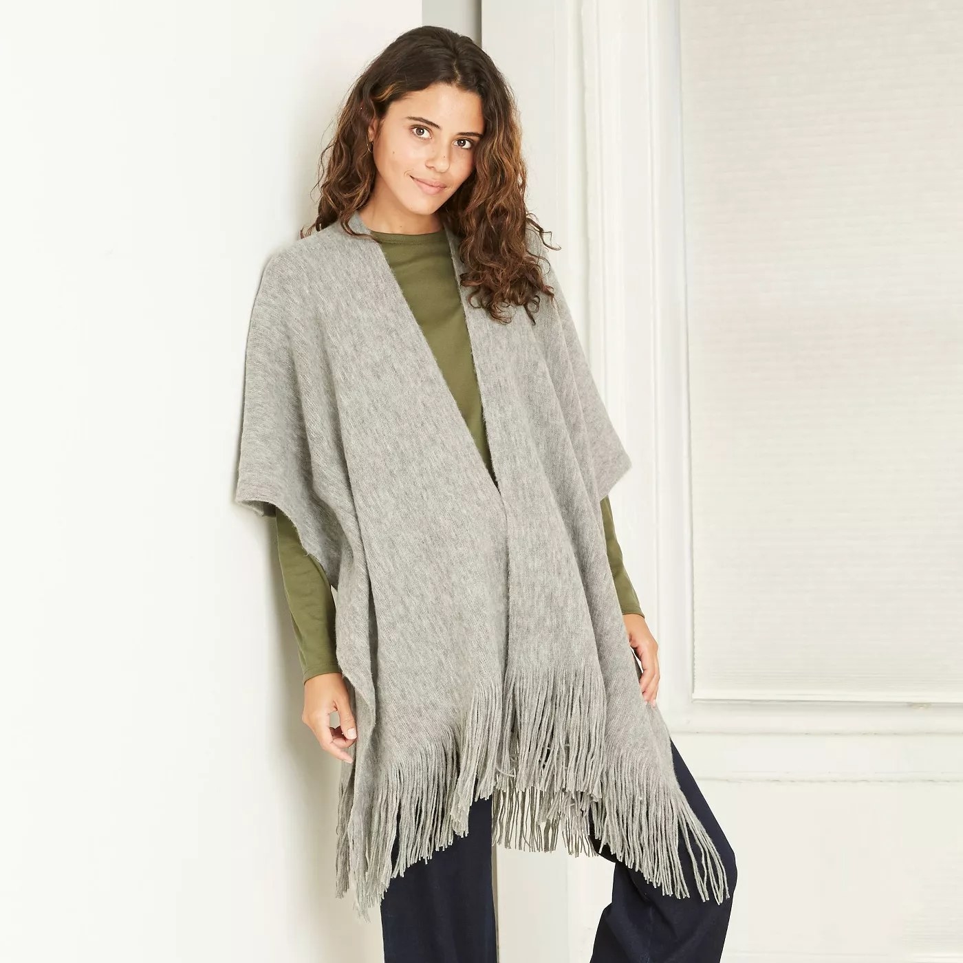 A gray knit poncho with fringe on the bottom.