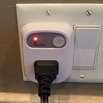 A photo of a black cord plugged into the time outlet with a small illuminated red light next to the words 