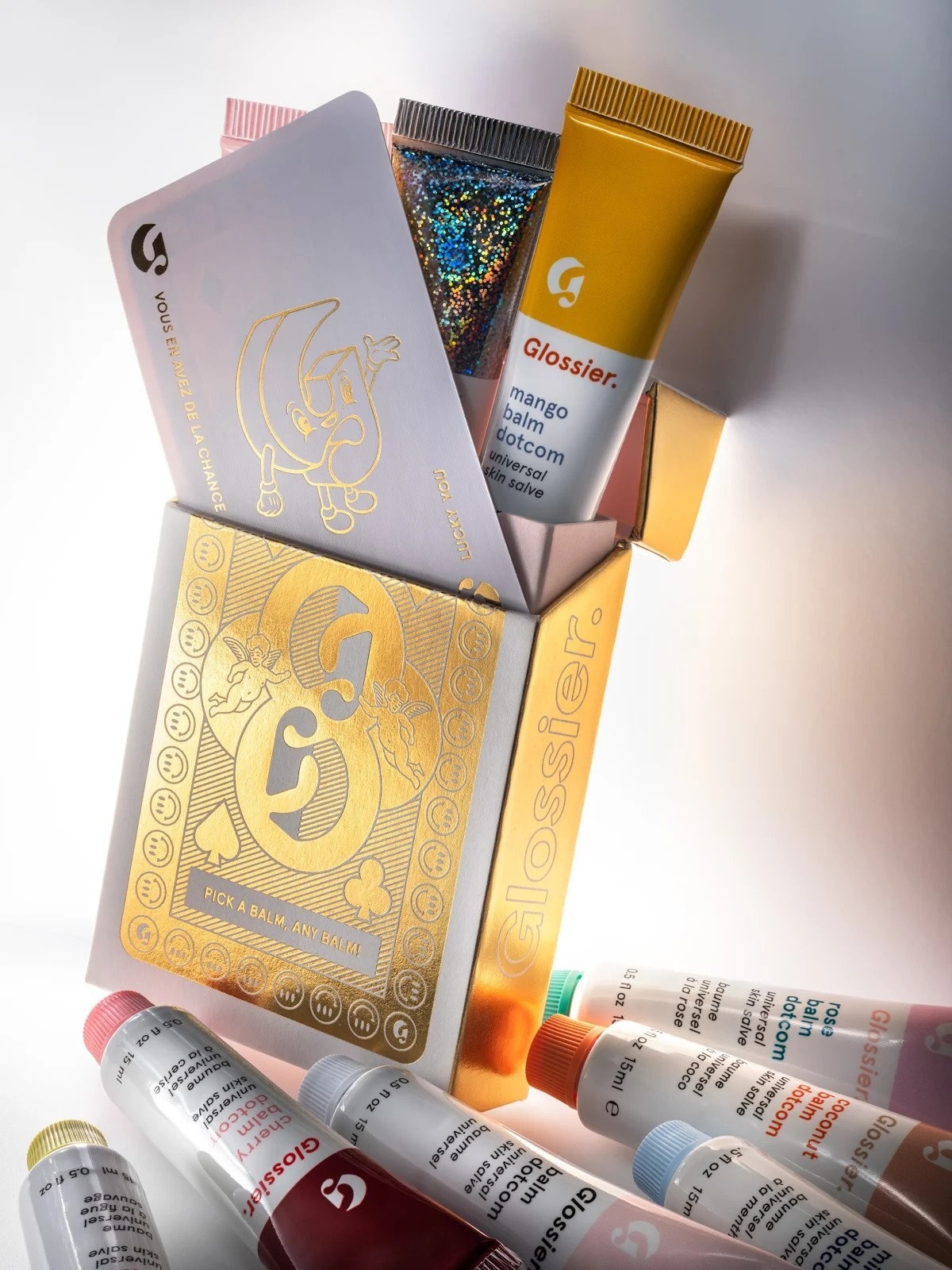 Gold and white Balm Dotcom Roulette gift box next to assorted Balm Dotcom tubes