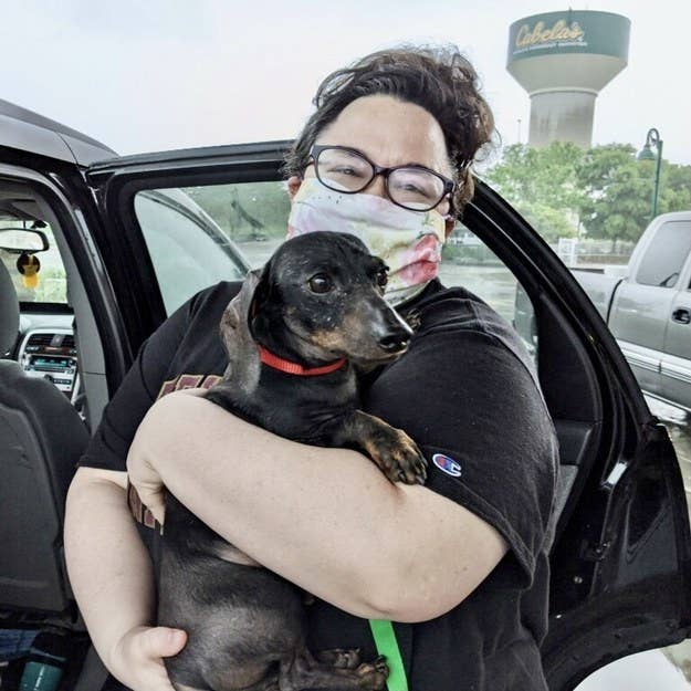 A women holding her new dog while wearing glasses and a mask next to her car