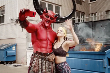 The Devil and a woman playing 2020 posing in front of a dumpster fire