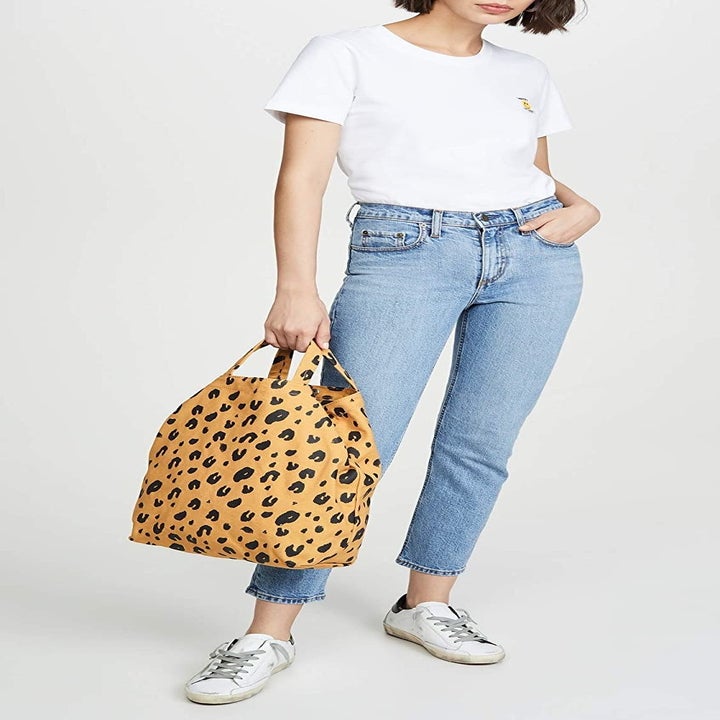 A model holding the yellow leopard print bag by the short handles