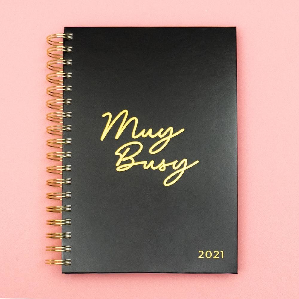 a black planner with a gold spiral spine that says &quot;Muy Busy&quot; on gold on the front