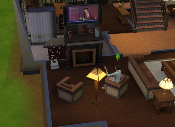 A Sim on a chair gesturing to the TV which shows a Sim