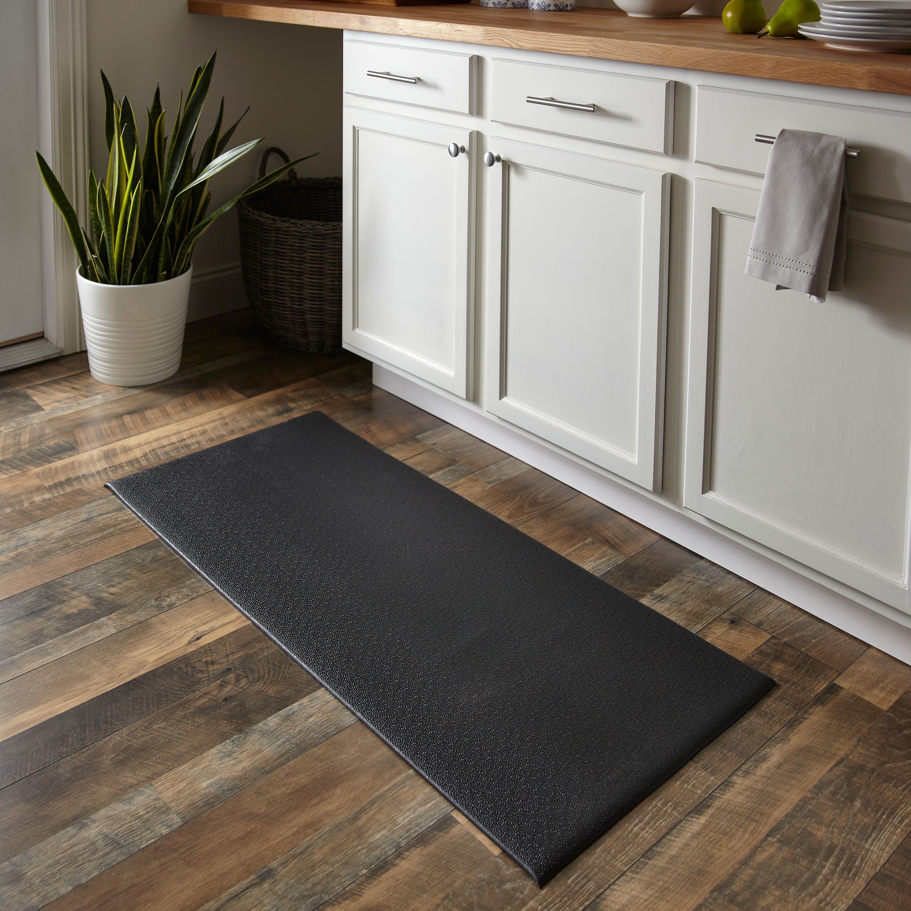 Black kitchen mat on a wooden floor, in front of white cabinets