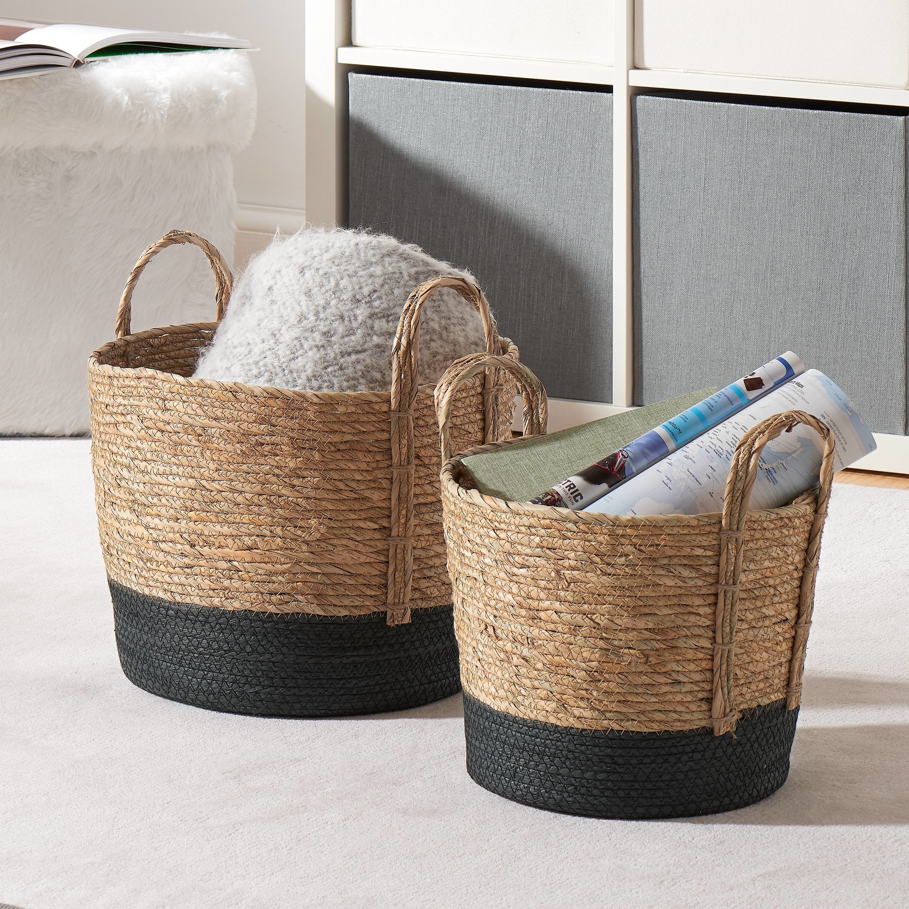 Two natural colored woven baskets with black bottoms and handles sitting on the floor