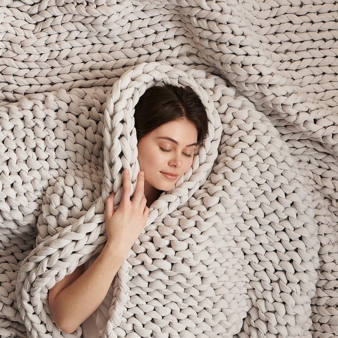 a model cuddled up in an ivory knit weighted blanket