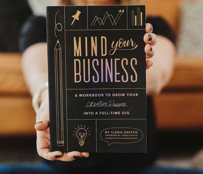 a person holding a copy of the book mind your business a workbook to grow your creative passion into a full-time gig