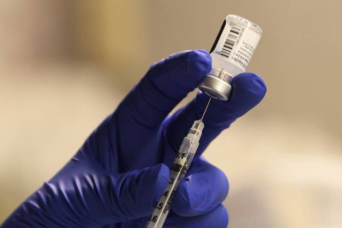A gloved hand inserts a syringe into a vial