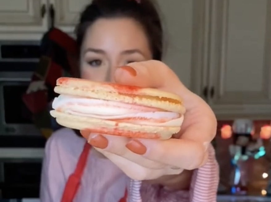 A woman holds a red and white swirled macaron with a white center