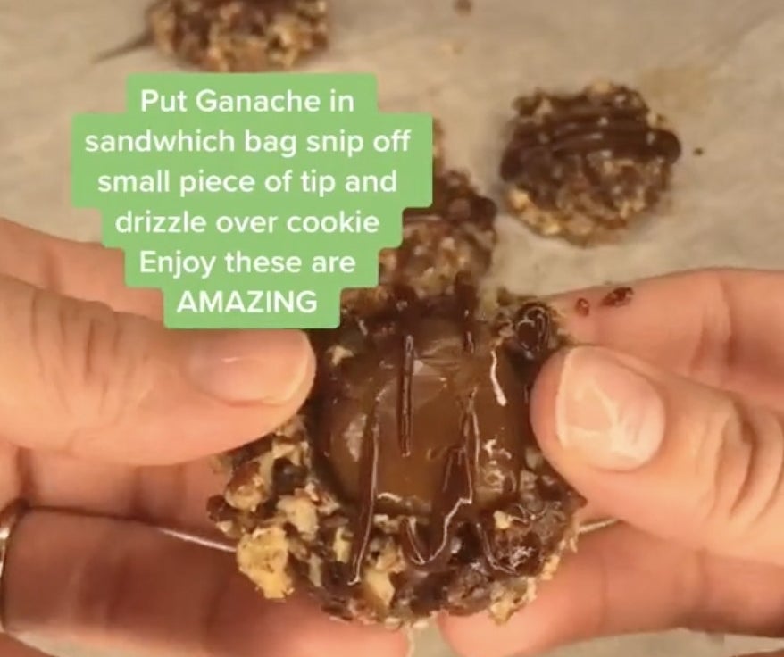 A pair of hands hold up a nutty cookie with chocolate drizzle