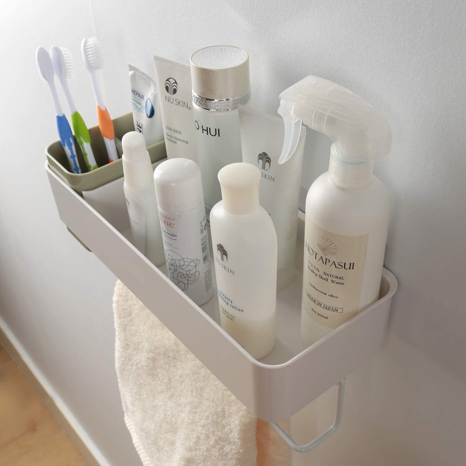 A wall mounted shelf with bathroom products, toothbrushes, and a towel hanging off it