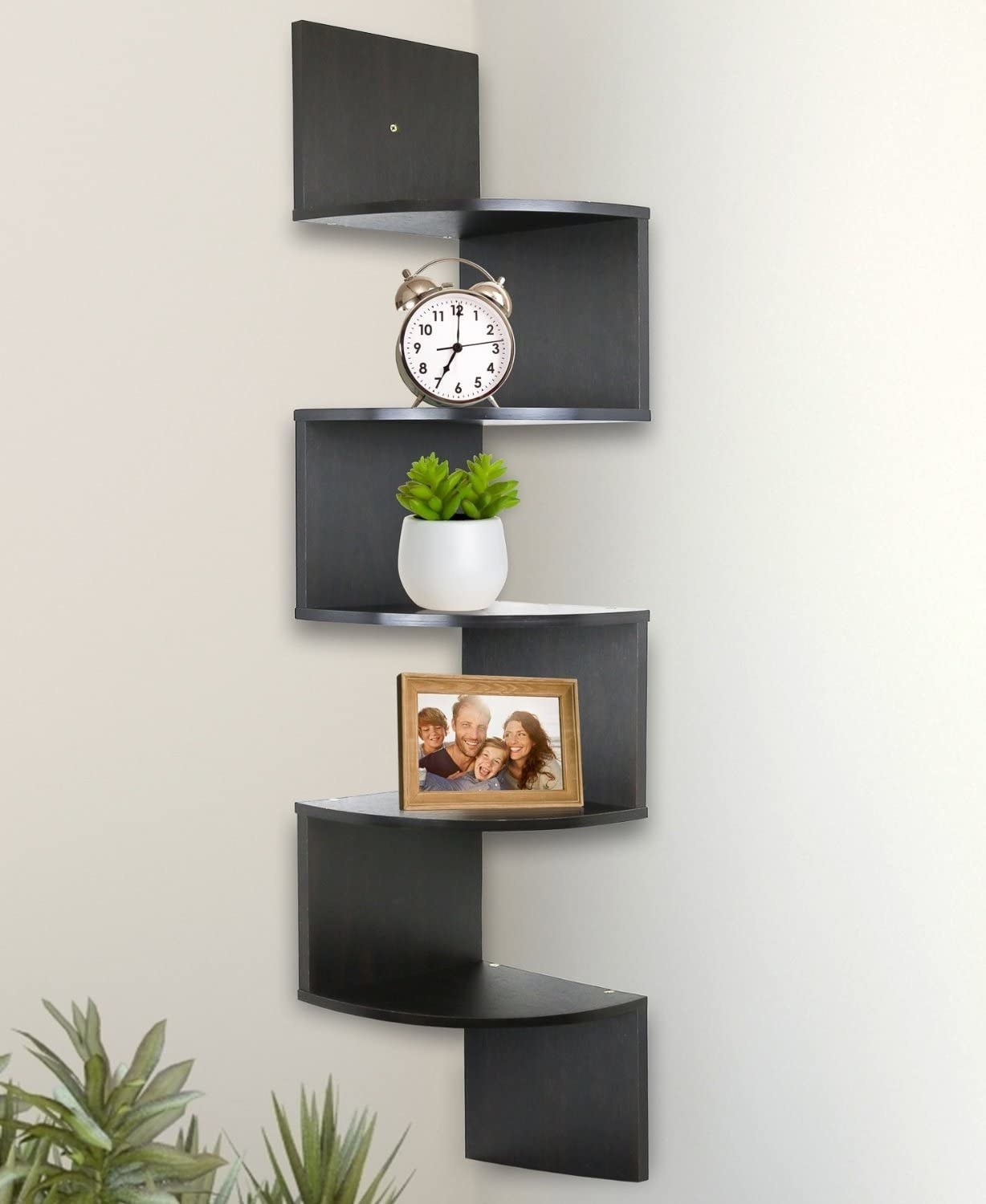 A corner shelf with a clock, plant, and picture frame on it
