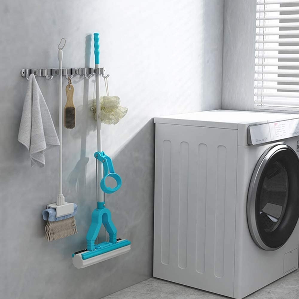 A towel, broom, brush, mop, and sponge hanging off the rack next to a washing machine