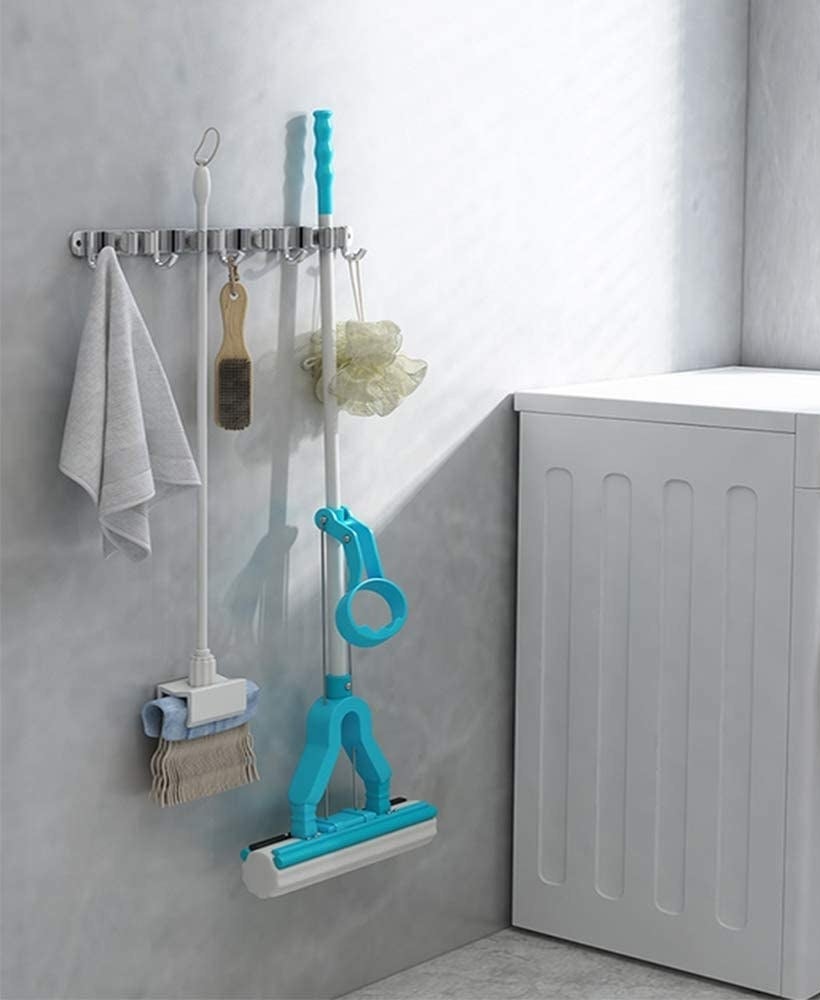 A towel, broom, brush, mop, and sponge hanging off the rack next to a washing machine