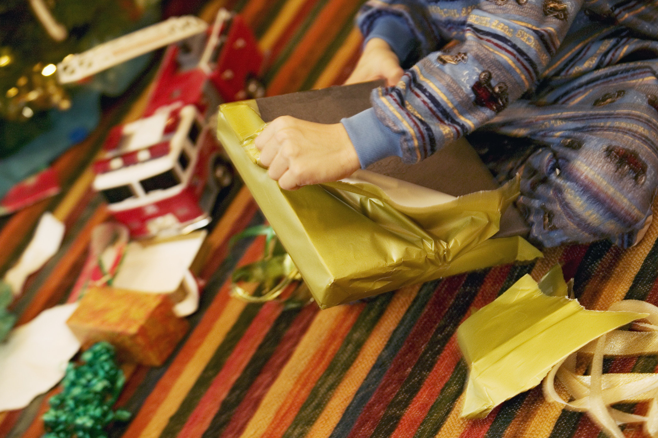 A close-up photo of a kid sitting on the floor opening a Christmas gift