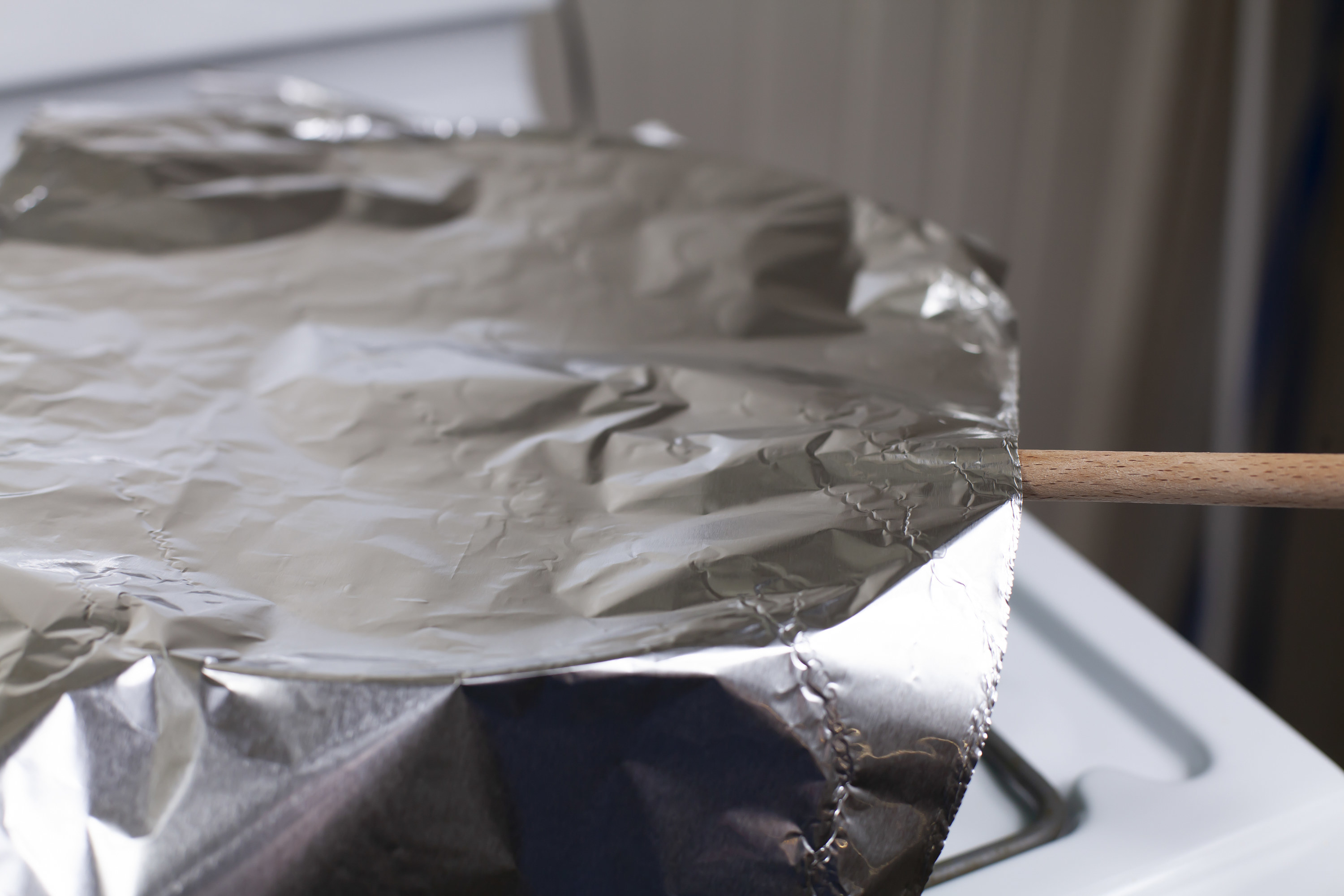 A pot on the stove with a wooden spoon in it and covered with foil
