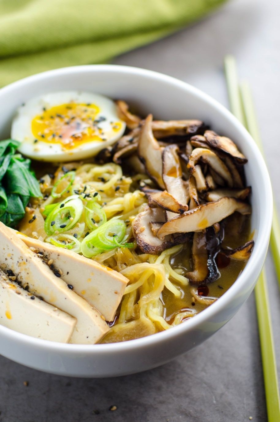 A bowl of vegetarian ramen with sliced tofu, mushrooms, scallions, and a soft boiled egg.