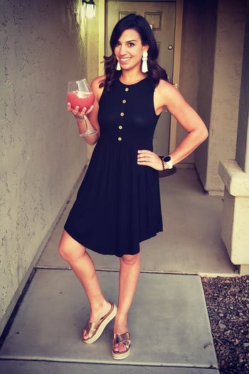 A reviewer wearing the sleeveless, above-the-knee dress with wooden buttons in black