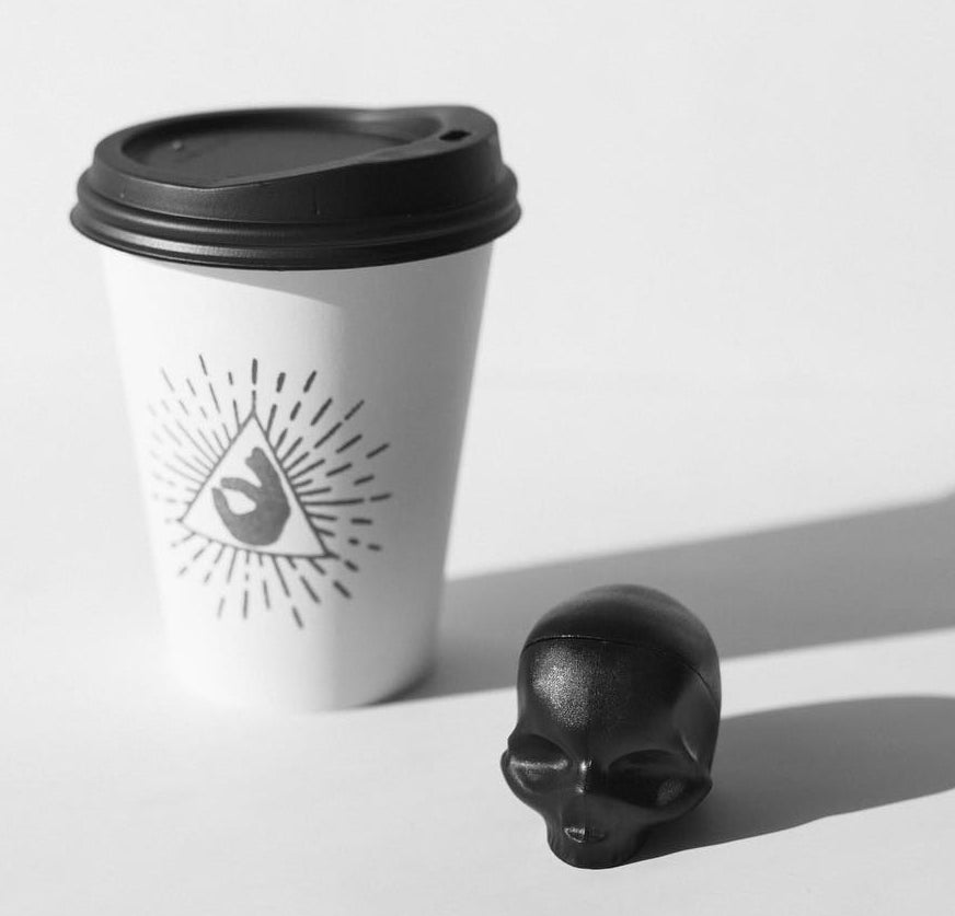 A skull-shaped lip balm next to a coffee cup