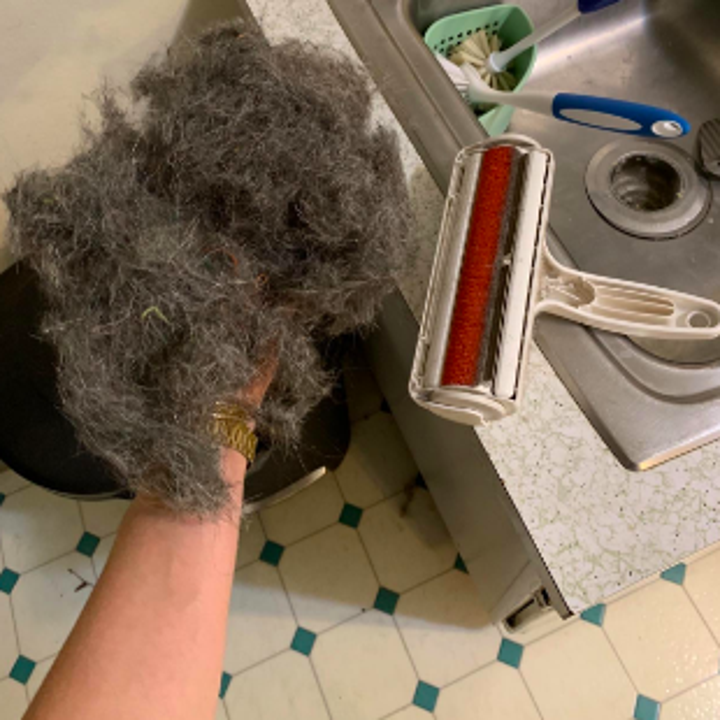 Person holding massive wad of pet fur with roller cleaner on table beside their hand 