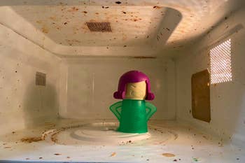 Microwave covered in caked on sauces and stains with steam cleaning tool inside 