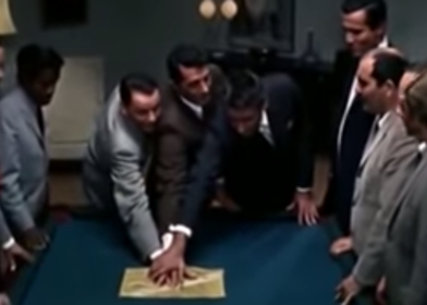 A group of men gather around a map sitting on a table in the movie "Ocean's Eleven."