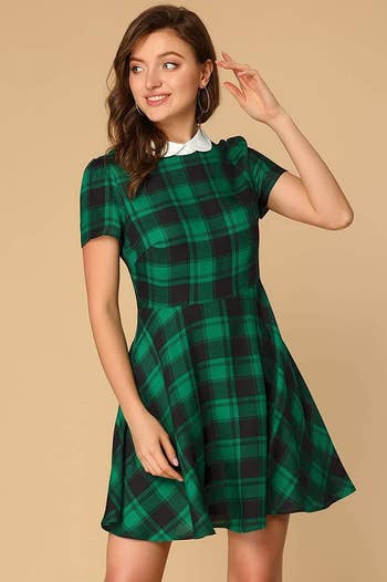 A model wearing the fit and flare, short-sleeve dress in green and black plaid with a white collar
