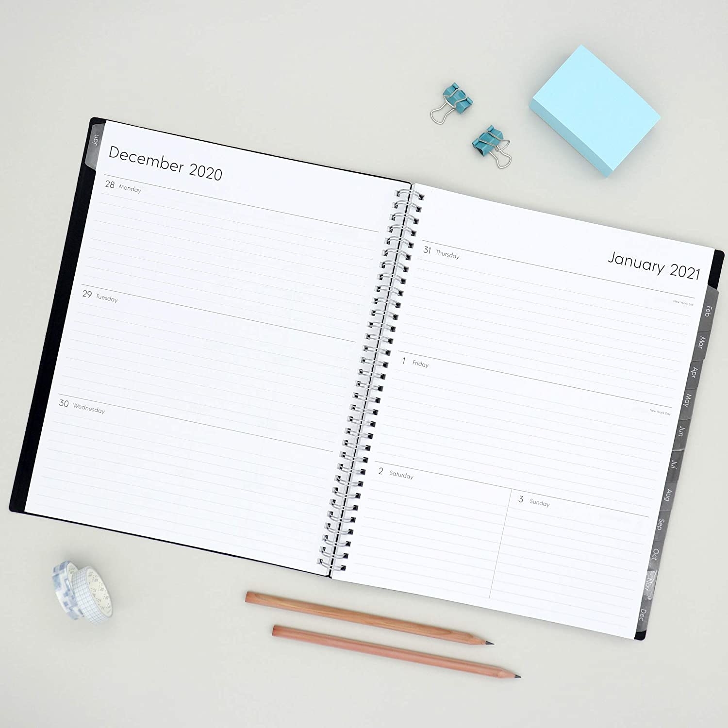 Black planner with lined date pages and tabs for each month on the side open on a desk 
