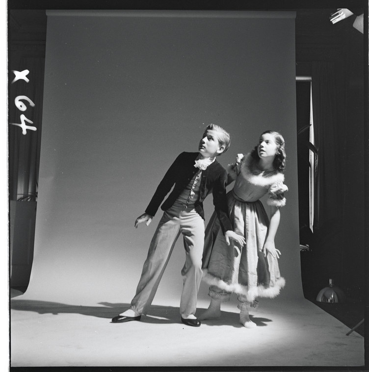 Two children in dance costumes looking offstage on a blank background