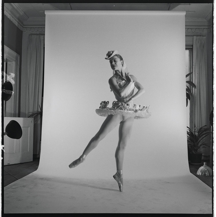 A woman ballerina in costume stands in front of a paper backdrop for a studio photo shoot