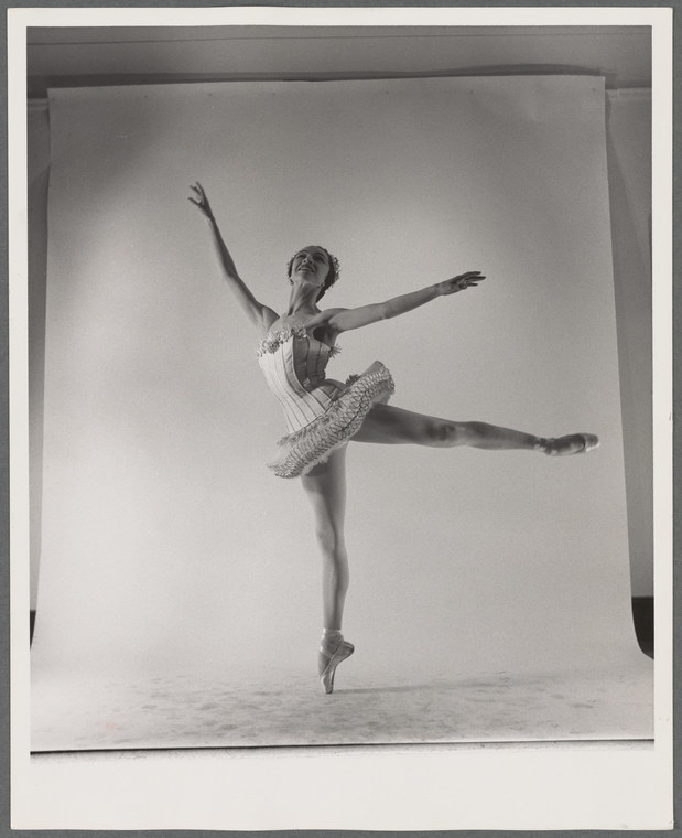 A ballet dancer wearing a frilly tutu with leg raised on a white backdrop