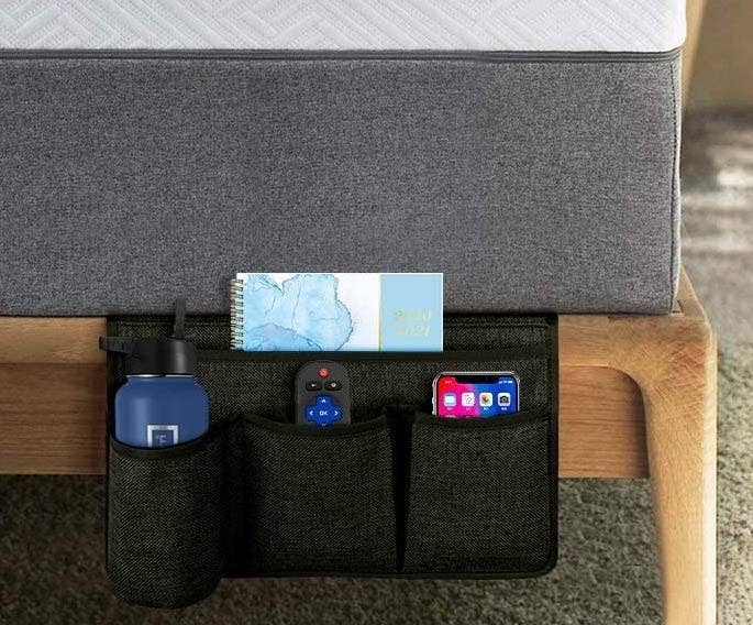 A bedside caddy with a waterbottle, journal, remote, and phone inside of it